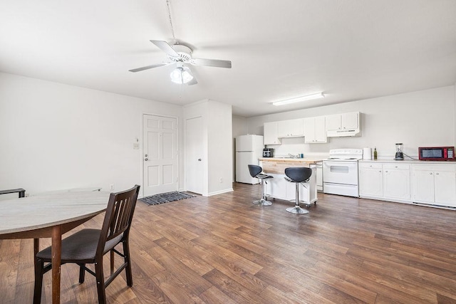 kitchen featuring a breakfast bar, white cabinetry, ceiling fan, dark wood-type flooring, and white appliances