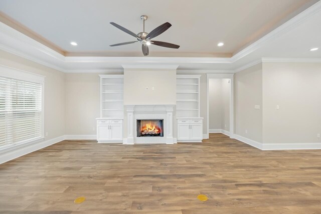 unfurnished living room with light wood-type flooring, a raised ceiling, ceiling fan, and crown molding