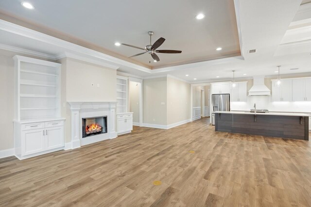 unfurnished living room with ornamental molding, a tray ceiling, and light hardwood / wood-style floors