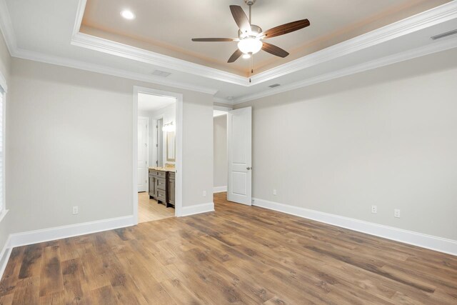 unfurnished bedroom featuring connected bathroom, ceiling fan, crown molding, a tray ceiling, and light hardwood / wood-style flooring