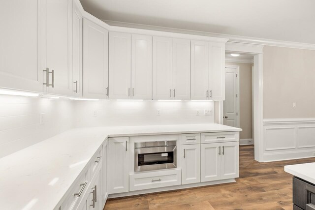 kitchen featuring wood-type flooring, crown molding, decorative backsplash, white cabinets, and oven