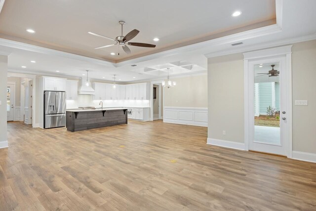 unfurnished living room with ceiling fan with notable chandelier, a raised ceiling, light wood-type flooring, and ornamental molding