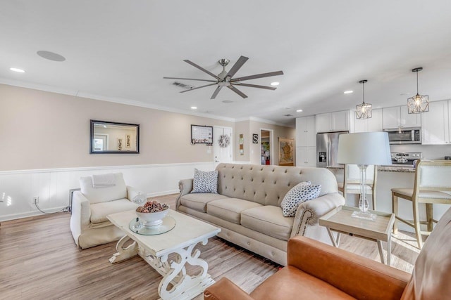 living room with ornamental molding, ceiling fan, and light wood-type flooring