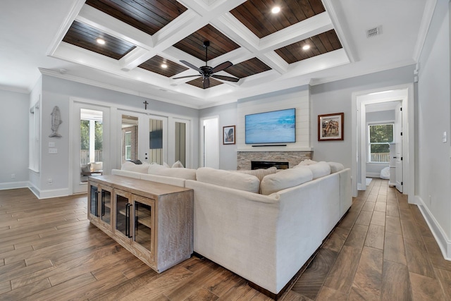 living room featuring crown molding, a stone fireplace, a wealth of natural light, and dark wood-type flooring