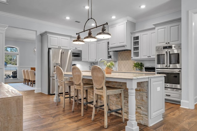 kitchen with appliances with stainless steel finishes, decorative light fixtures, a kitchen breakfast bar, and an island with sink