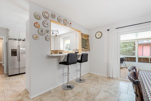 kitchen with tasteful backsplash, baseboards, stainless steel fridge with ice dispenser, a kitchen bar, and white cabinets