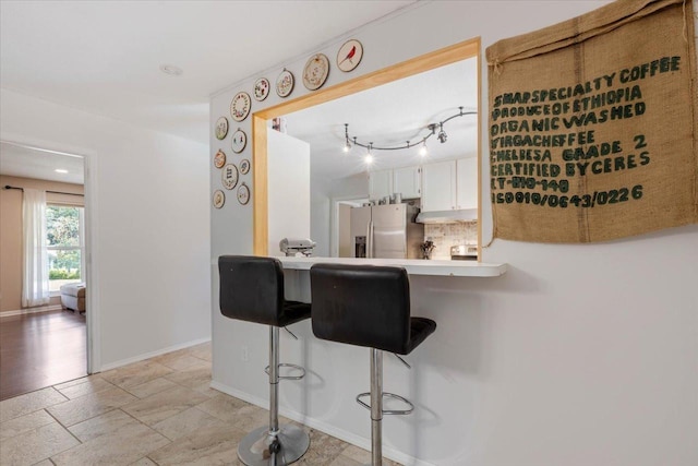 kitchen featuring backsplash, baseboards, a breakfast bar, light countertops, and stainless steel refrigerator with ice dispenser