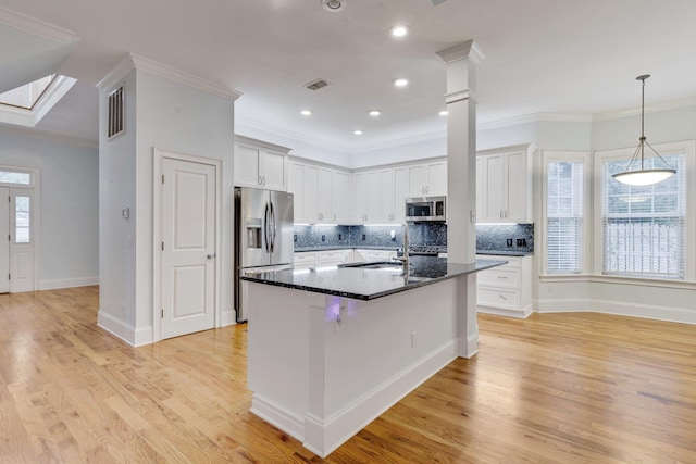 kitchen with appliances with stainless steel finishes, a kitchen island with sink, white cabinetry, dark stone countertops, and light wood-type flooring
