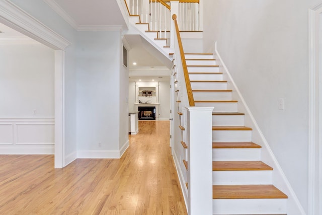 stairs featuring ornamental molding, a fireplace, a decorative wall, and wood finished floors
