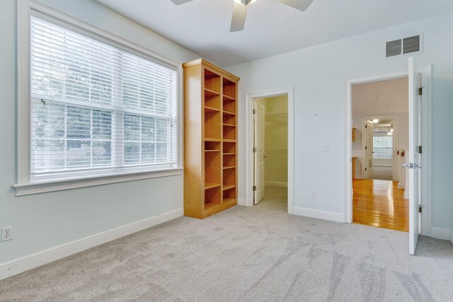 unfurnished bedroom featuring light colored carpet, a walk in closet, visible vents, and baseboards