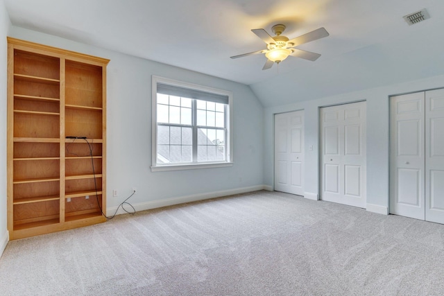 unfurnished bedroom with light colored carpet, visible vents, multiple closets, vaulted ceiling, and baseboards