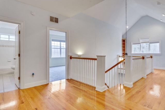 corridor featuring light wood-type flooring, visible vents, plenty of natural light, and an upstairs landing