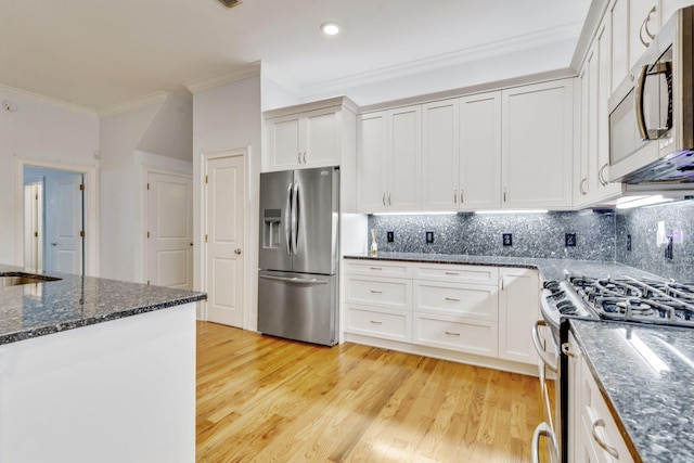 kitchen with crown molding, light wood finished floors, stainless steel appliances, white cabinetry, and dark stone counters