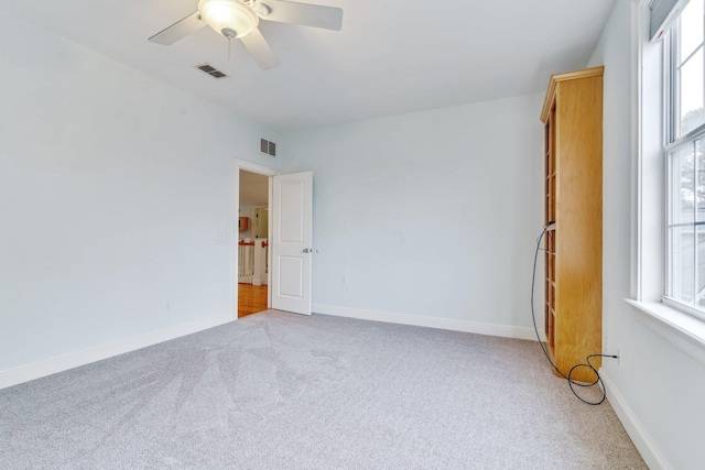 spare room with light carpet, baseboards, visible vents, and ceiling fan