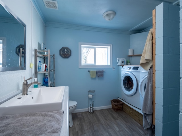 clothes washing area featuring laundry area, visible vents, washer / clothes dryer, wood finished floors, and a sink