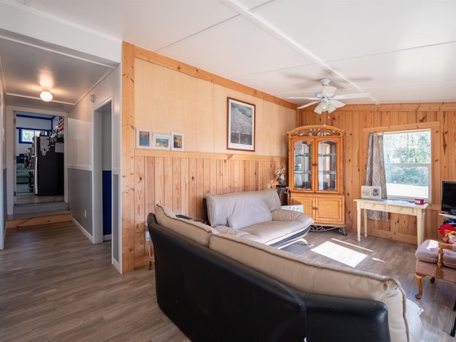 living area featuring a ceiling fan, wooden walls, and wood finished floors