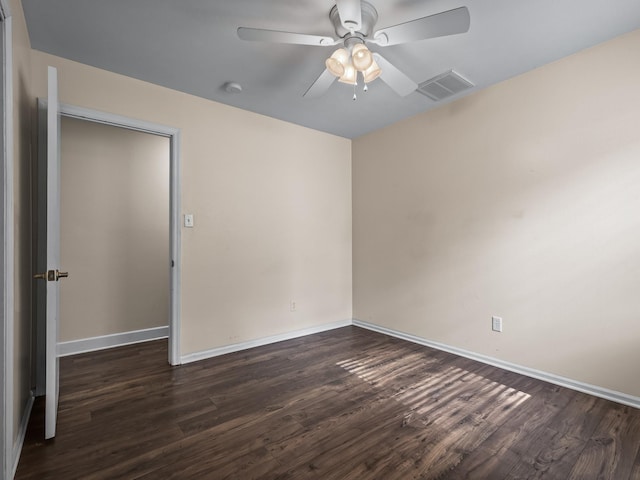 unfurnished room with dark wood-style floors, visible vents, a ceiling fan, and baseboards