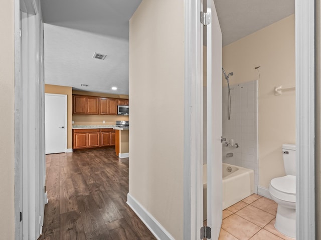 bathroom with shower / bath combination, toilet, visible vents, baseboards, and wood finished floors