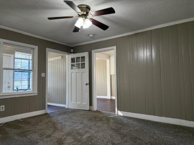 carpeted spare room featuring crown molding, wooden walls, ceiling fan, and a textured ceiling