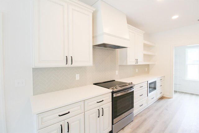 kitchen with stainless steel appliances, white cabinets, tasteful backsplash, custom range hood, and light hardwood / wood-style flooring