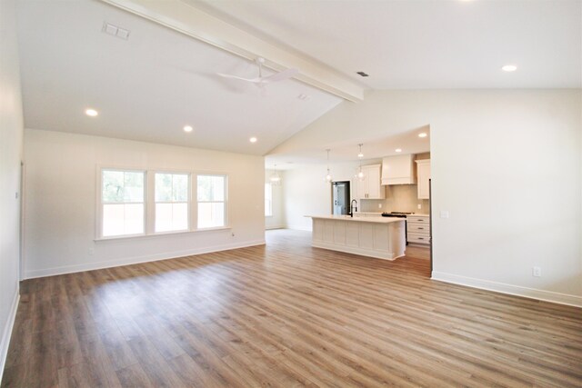 unfurnished living room with light hardwood / wood-style floors, ceiling fan, sink, and lofted ceiling with beams