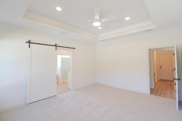 unfurnished bedroom featuring connected bathroom, a tray ceiling, a barn door, and ceiling fan