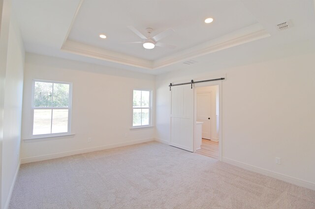 carpeted empty room with a tray ceiling, a barn door, and plenty of natural light