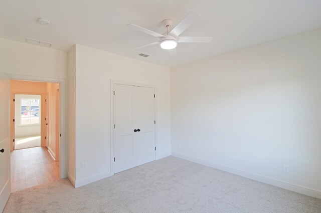 unfurnished bedroom with a closet, light colored carpet, and ceiling fan