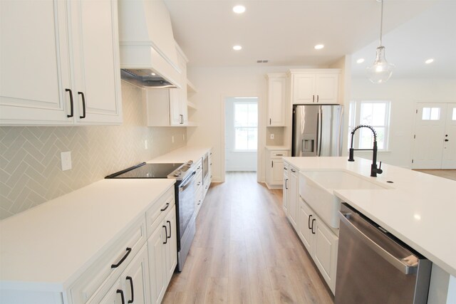 kitchen featuring light hardwood / wood-style floors, appliances with stainless steel finishes, premium range hood, white cabinets, and pendant lighting