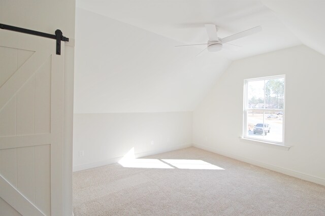 additional living space featuring light carpet, a barn door, vaulted ceiling, and ceiling fan