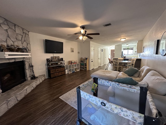 living room featuring ceiling fan, dark hardwood / wood-style floors, and a stone fireplace