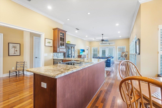 kitchen with dark wood-type flooring, crown molding, light stone countertops, and tasteful backsplash