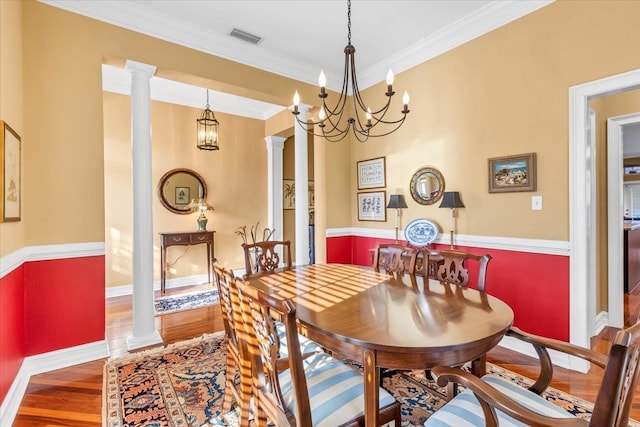 dining area with decorative columns, crown molding, hardwood / wood-style floors, and an inviting chandelier