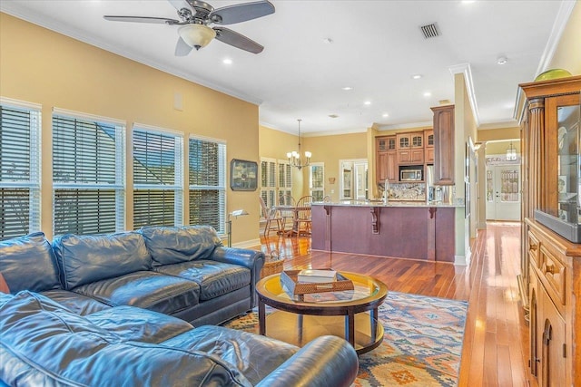 living room featuring ceiling fan with notable chandelier, ornamental molding, and light hardwood / wood-style floors