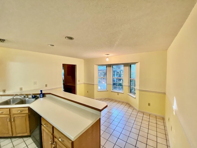 kitchen featuring light tile patterned floors, a peninsula, a sink, light countertops, and brown cabinetry