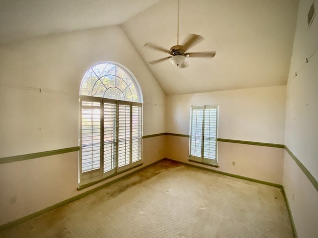 empty room with lofted ceiling, ceiling fan, baseboards, and light colored carpet