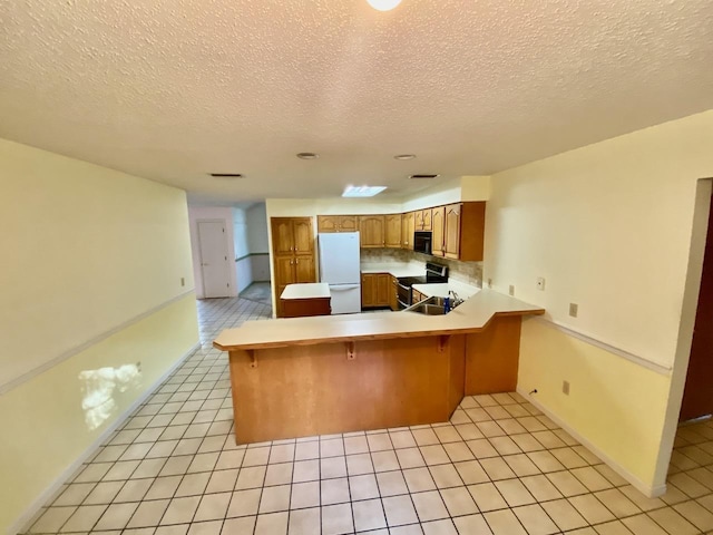 kitchen with range with two ovens, a peninsula, light countertops, freestanding refrigerator, and brown cabinets