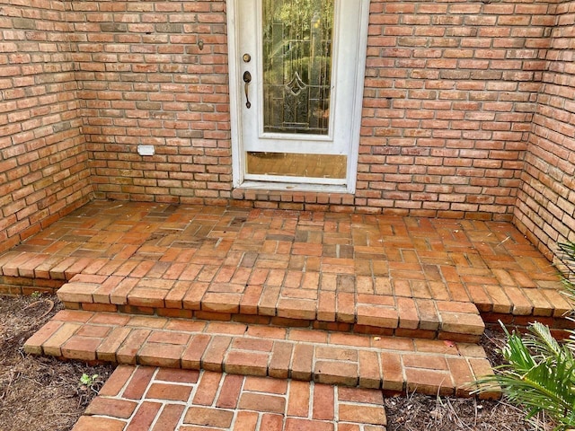 property entrance with a patio area, a shingled roof, and brick siding