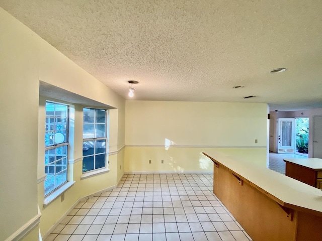 empty room with light tile patterned flooring, a textured ceiling, and baseboards