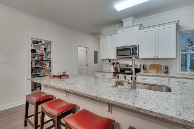 624 W 7th Ave, Tallahassee, FL 32303 - kitchen with stainless steel appliances, crown molding, white cabinets, a kitchen bar, and light wood-style flooring
