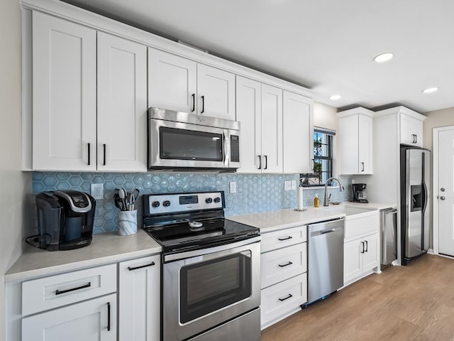 kitchen featuring white cabinets, light wood-type flooring, stainless steel appliances, and tasteful backsplash