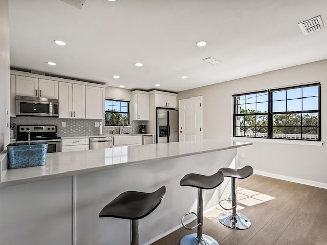 kitchen with a breakfast bar area, white cabinetry, stainless steel appliances, and light wood-type flooring