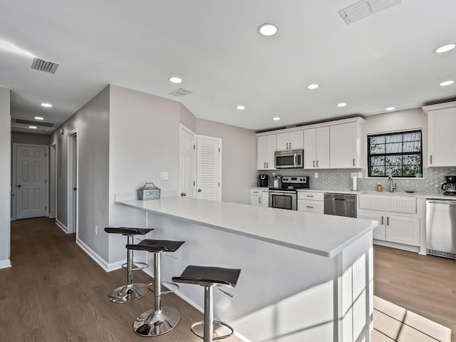 kitchen with white cabinets, appliances with stainless steel finishes, wood-type flooring, and sink