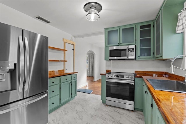 kitchen with wood counters, green cabinets, sink, and appliances with stainless steel finishes