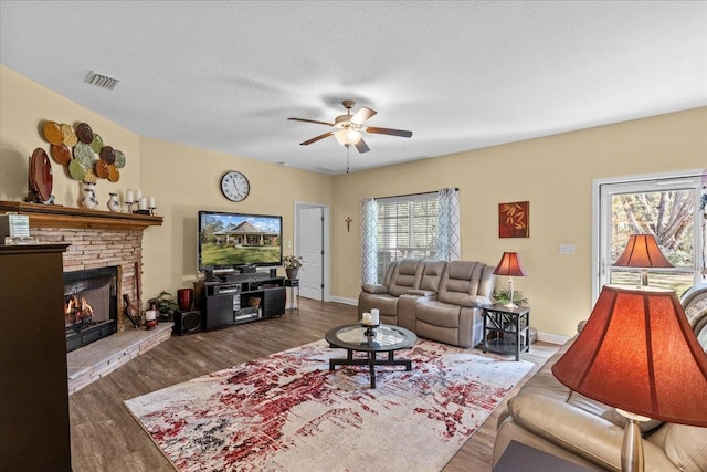 living room with dark hardwood / wood-style floors, ceiling fan, a textured ceiling, and a brick fireplace