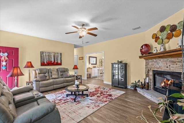 living room featuring a textured ceiling, a fireplace, ceiling fan, and dark wood-type flooring