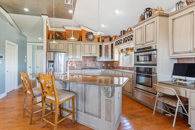 kitchen featuring light wood-type flooring, stainless steel appliances, vaulted ceiling, hanging light fixtures, and an island with sink