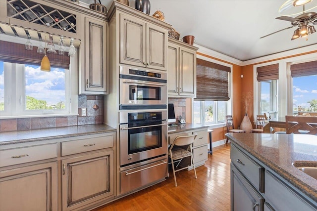 kitchen with decorative backsplash, plenty of natural light, stainless steel double oven, and light wood-type flooring