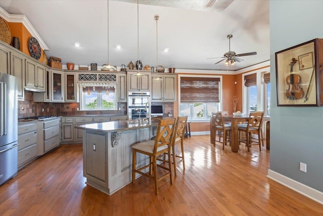 kitchen with hardwood / wood-style flooring, decorative light fixtures, decorative backsplash, a center island with sink, and appliances with stainless steel finishes