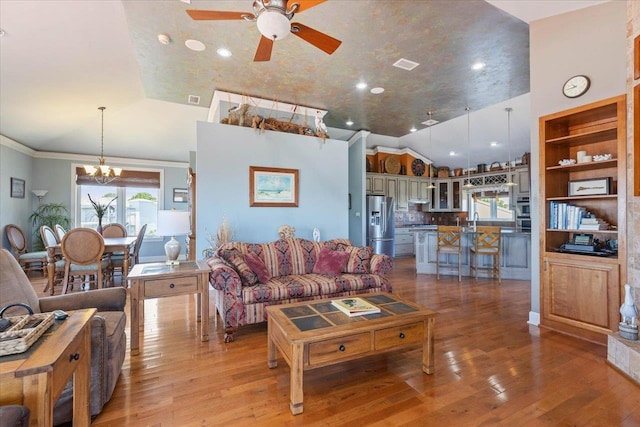 living room with hardwood / wood-style floors, high vaulted ceiling, ceiling fan with notable chandelier, sink, and ornamental molding